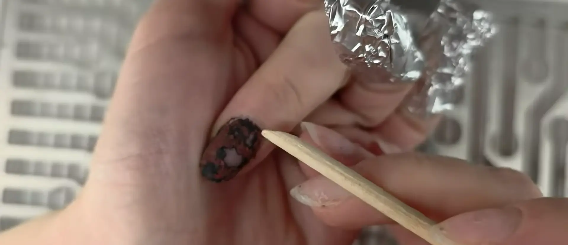 Proper technique for gently scraping softened gel polish with orange wood stick showing crumbly texture