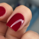 Close-up of a finished Russian manicure with a glossy deep red finish on a short natural nail
